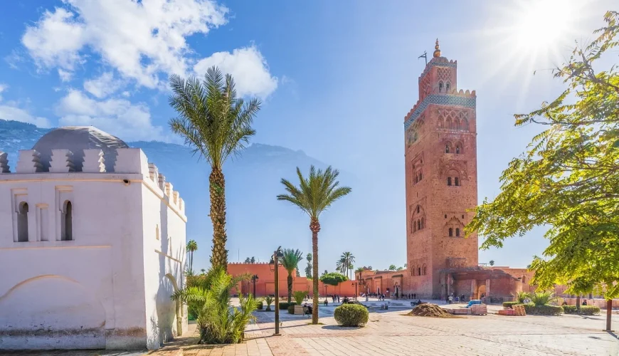 Majestic view of Koutoubia Mosque in Marrakech at sunset, with its iconic minaret towering against a pink and orange sky, surrounded by lush gardens